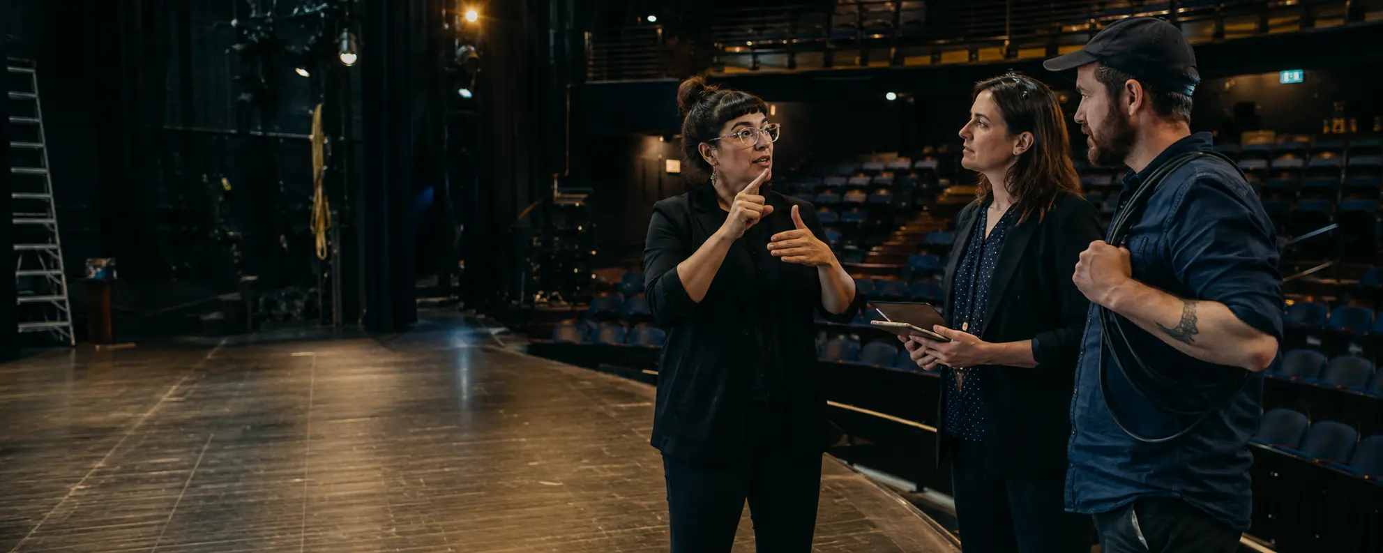 Three people discussing stage access in an empty performance space